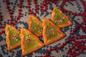 This Christmas background: beautiful cookies in the form of Christmas trees and beads lie on a warm scarf. The concept of Christmas and new year holidays.
