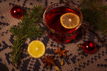 New year Christmas background. This is a glass Cup filled with a red drink with a slice of lemon, standing on a warm scarf, Christmas decorations, cardamom, star anise.