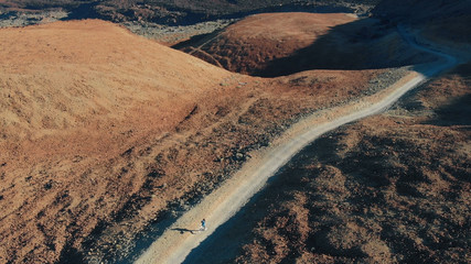 Aerial view. A young hipster girl runs in the mountains on a pedestrian route to the volcano.