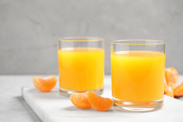 Glasses of fresh tangerine juice and fruits on light table