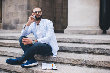 Content male relaxing on street and communicating on mobile