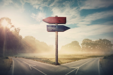 Surreal landscape with a split road and signpost arrows showing two different courses, left and right direction to choose. Road splits in distinct direction ways. Difficult decision, choice concept. - 310014089