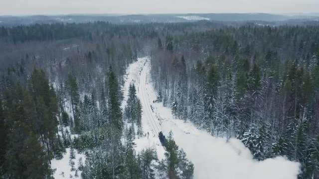 Aerial view steam retro train in snowy spruce forest. Follow shot above peak of trees