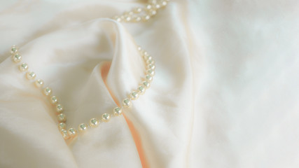Defocused luxury silk background with a string of pearls. Delicate pastel shade. Pastel colors, concept of comfort and sexuality.