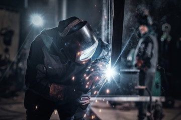 Man is working at metal factory, he is welding a piece of rail using special tools. - obrazy, fototapety, plakaty