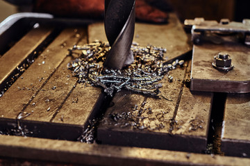 Drilling hole in the metal with giant drill at steel factory by worker male.