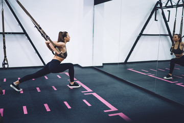 Young attractive athletic female training with trx straps in gym