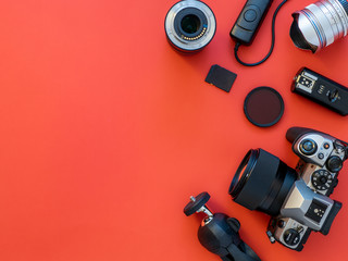 Photographer workplace with dslr camera, lens, pen tablet and camera accessories on red background....