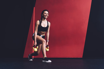 Cheerful young sporty woman working out with kettlebells in fitness center