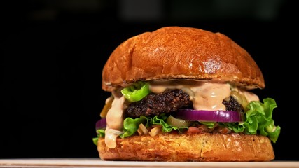 Craft burger is cooking on black background. Consist: red sauce salsa, lettuce, red onion, pickle,...