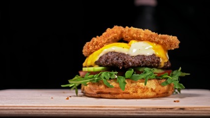 Craft burger is cooking on black background in black food gloves. Consist: sauce, arugula, tomato, red onion rings fries, cucumber, cheese, air bun and marble meat beef. Not made ideal. Looks real