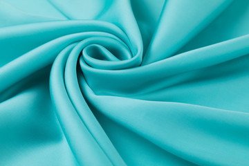 The blue satin fabric is laid out on the table in a spiral view. Soft folds of a drapery, Silky surface