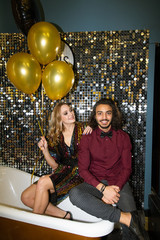 Young woman with bunch of balloons looking at her happy boyfriend at party