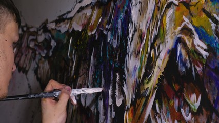 Artist designer draws an eagle on the wall. Craftsman decorator paints a picture with acrylic oil color. Painter painter dressed in a paint coat. Indoor. Dark magic cinematic look.