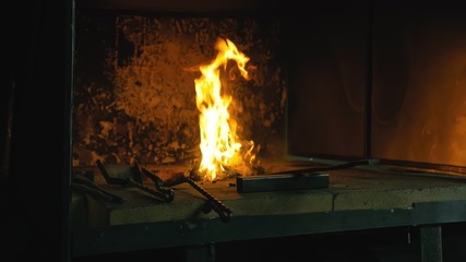 Forge fire in furnace. Blacksmith tempers a steel product in a stove. Smithy forging for hardening...