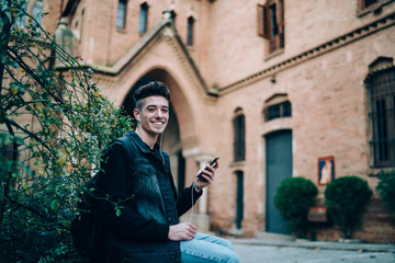 Young man with earphones sitting using smartphone