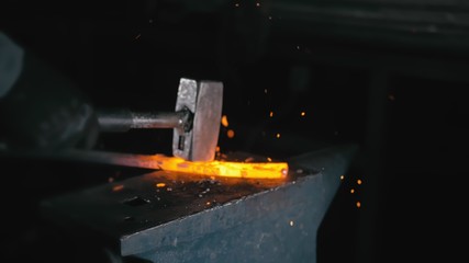 Forge workshop. Smithy manual production. Hands of smith with hammer hit on glowing hot metal, on...