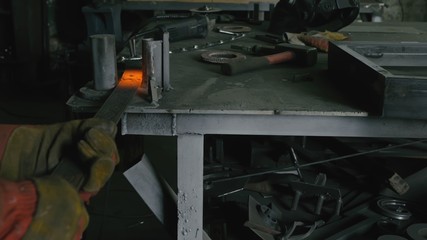 Forge workshop on table. Smithy manual production. Work on the product. Ruler, angle grinder. Worker rules and bends metal part. The blacksmith manufacture of fireplaces, stoves.