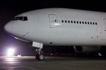 Close-up taxiing white wide body passenger aircraft at night in the rain