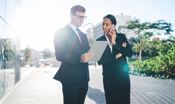 Collaborating young man and woman with gadgets
Elegant male assistant showing tablet with young African American woman speaking on mobile phone standing together on street in sunlight