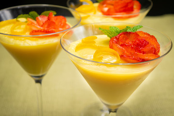 Vanilla Pudding with lemon and strawberry garnish in Martini glass with black background.