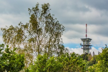 Obraz premium Zelena hora, Pelhrimov / Czech Republic - September 13 2019: Distant view of television communication tower with satellite dishes on. Cloudy sky. Green trees in foreground.