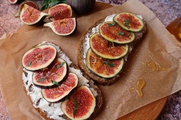 Figs. Sandwiches with figs, cheese, arugula, honey and nuts on wooden board over textured purple backdrop. Homemade. Everyday autumn kitchen.