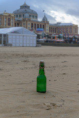 Lonely green beer bottle with sand on it, left on the beach of Scheveningen. In the background the buildings on the boulevard.