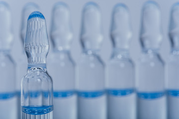Glass medical ampoule vial for injection. Medicine is liquid sodium chloride with of aqueous solution in ampulla. Close up. Bottles ampule multicolor on background color and water. Human plasma.