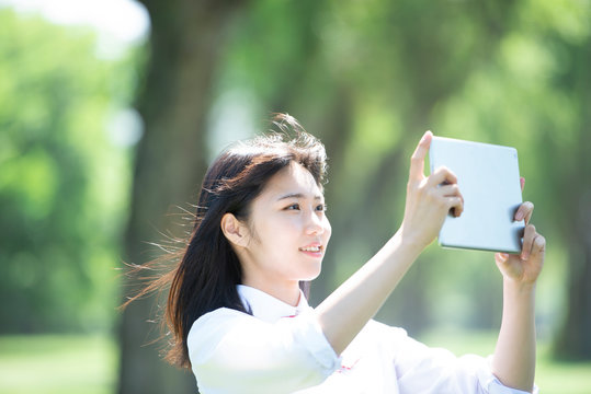 ポプラ並木でタブレットPCを持つ女子学生