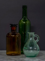 Green and Brown Glass Bottles with Jar on Marble table with Black Background Still