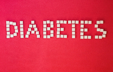 word diabetes, healthcare concept, made of refined loaf sugar cubes on red backround.