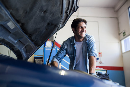 Smiling man working with engine of car in repair service and looking away