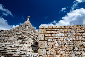 Fototapeta na wymiar Roofs of truli, typical whitewashed cylindrical houses in Alberobello, Puglia, Italy with amazing blue sky with clouds and old stone beautiful masonry wall