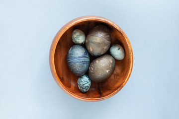 Creatively painted chicken and quail Easter eggs with natural hibiscus dye, look like sea stones in bowl on a gray background. Happy Easter DIY concept. Soft slective focus. Flat lay