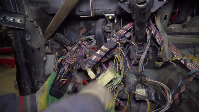 auto mechanic parses a car in a garage. He cuts the wire with scissors. Car on auto parts.