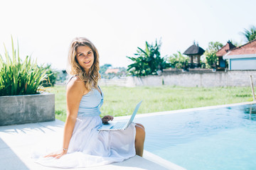 Smiling woman relaxing on edge of pool with laptop