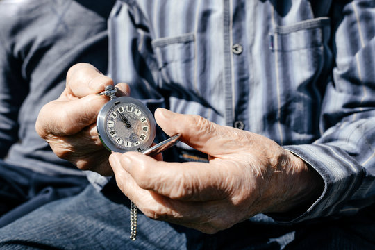 Old man's hands holding silver pocket clock, close-up