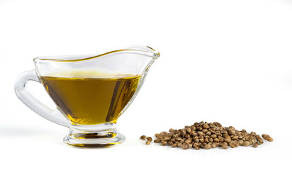 Hemp oil in a glass gravy boat with a bunch of marijuana seeds. Isolated on white background.