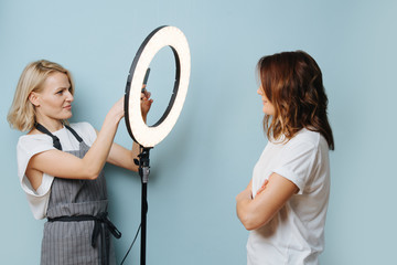 Lady hairdresser is taking photo of a client with the help of ring lamp