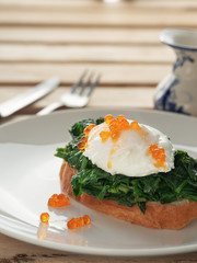 Poached egg with red caviar, fried spinach on white bread toast. Close-up. Tasty breakfast. Vertical orientation.