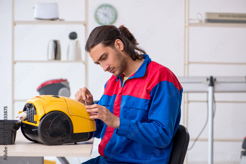 Wall mural young male contractor repairing vacuum cleaner at workshop