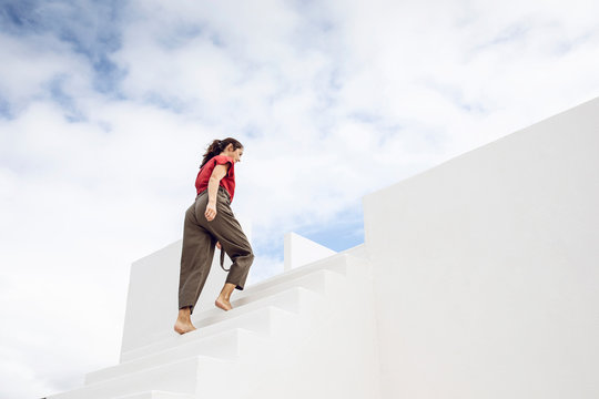Barefooted businesswman climbing white stairs under cloudy sky