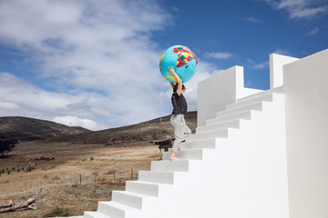 Little girl on white stairs, carrying inflatable globe