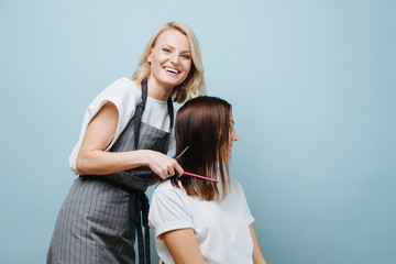 Cheerful blonde female hairdresser combing client's hair over blue background.