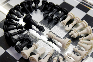 black and white chess pieces folded in a circle lie on a mirrored chess board with a black and white king in the center of the circle