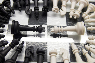 black and white chess pieces folded in a circle lie on a mirrored chess board with a black and white king in the center of the circle