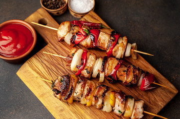 Skewers of meat with grilled vegetables on a cutting board on a stone background