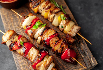 Skewers of meat with grilled vegetables on a cutting board on a stone background