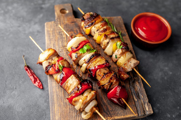 Skewers of meat with grilled vegetables on a cutting board on a stone background